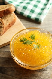 Fresh pike caviar in bowl and bread on wooden table, closeup