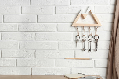 Photo of Wooden key holder on white brick wall indoors. Space for text