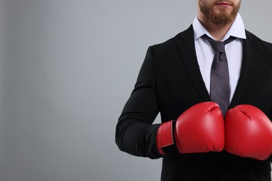 Photo of Businessman in suit wearing boxing gloves on grey background, closeup. Space for text