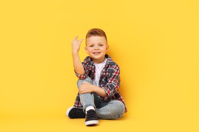 Happy little boy sitting on yellow background