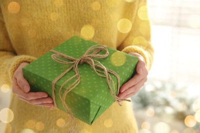 Photo of Woman holding green Christmas gift box indoors, closeup