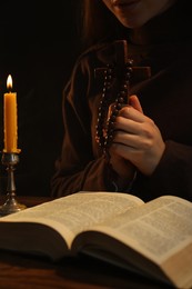 Photo of Woman praying at table with burning candle and Bible, closeup