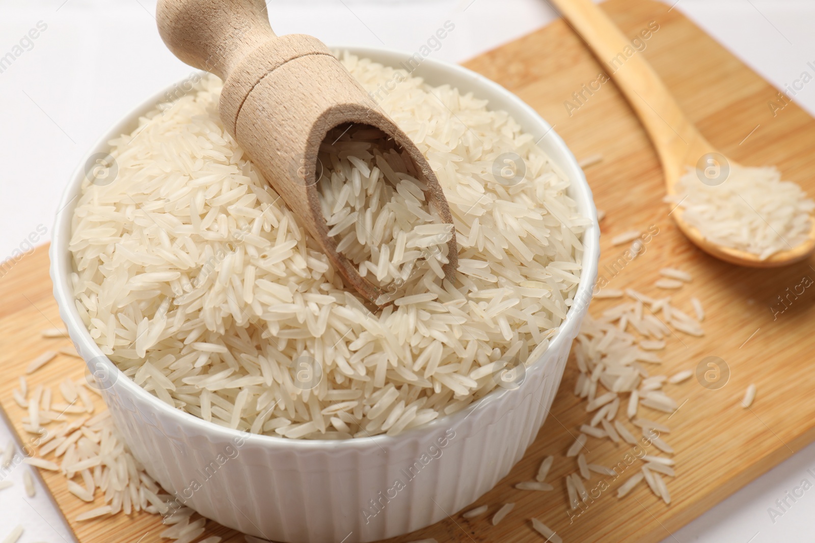 Photo of Raw basmati rice in bowl, scoop and spoon on white table, closeup