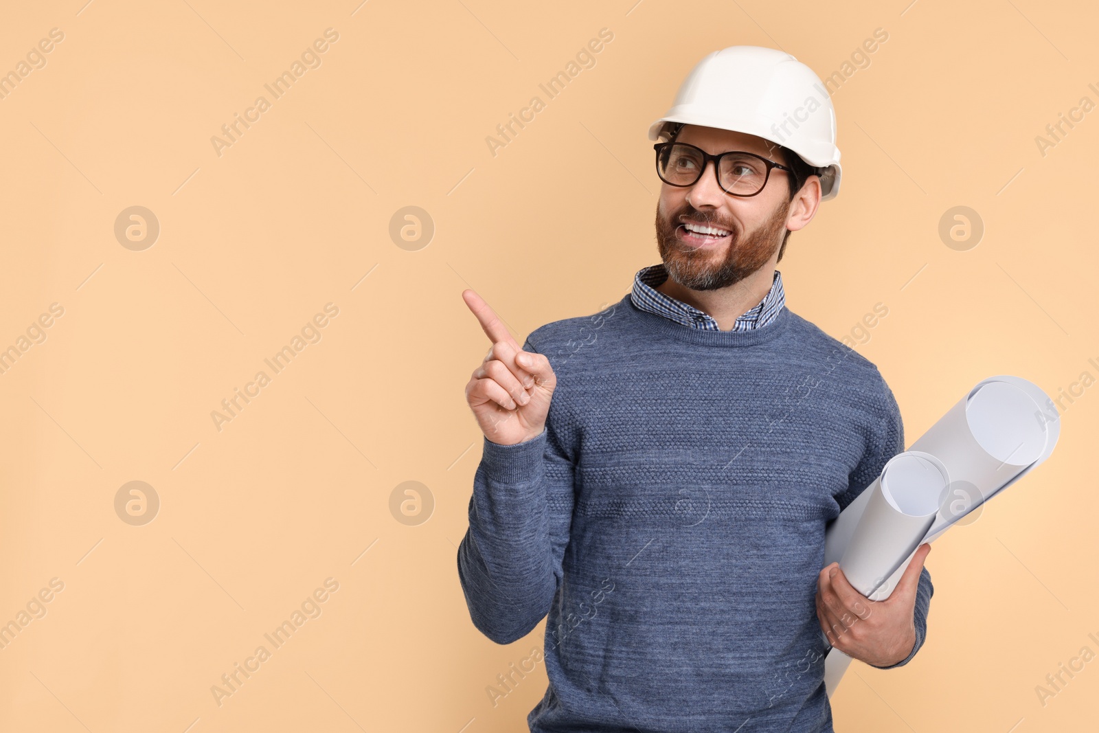 Photo of Architect in hard hat with drafts pointing at something on beige background