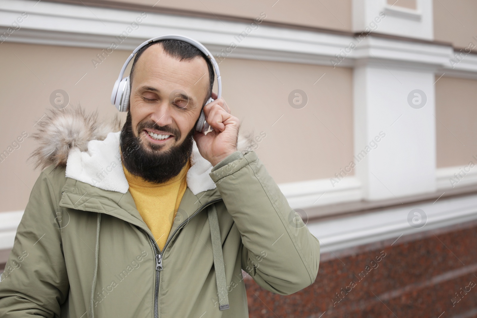 Photo of Mature man with headphones listening to music near light wall. Space for text