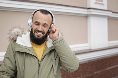 Mature man with headphones listening to music near light wall. Space for text