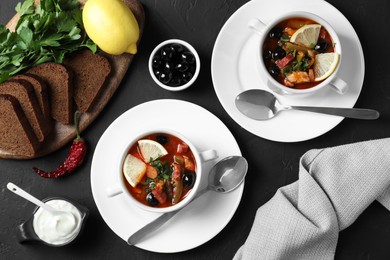 Photo of Meat solyanka soup with sausages, olives and vegetables served on dark grey textured table, flat lay