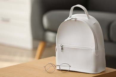 Photo of Stylish white backpack and glasses on wooden table indoors, space for text