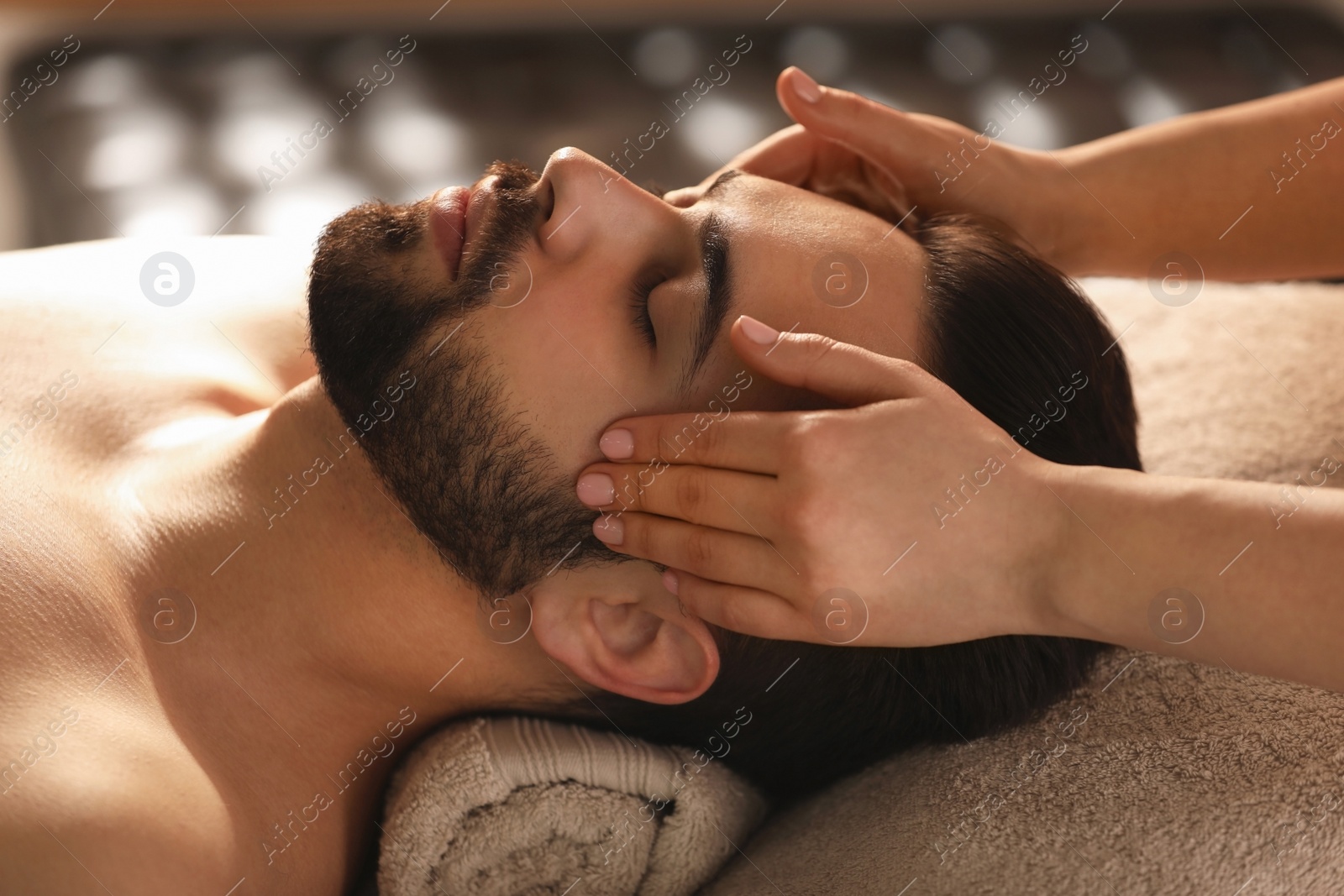 Photo of Young man receiving facial massage in beauty salon
