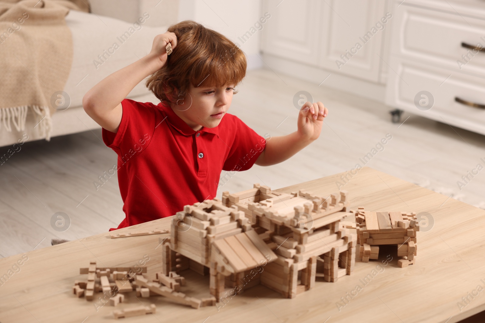 Photo of Cute little boy playing with wooden construction set at table in room. Child's toy