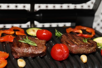 Photo of Electric grill with tasty meat, spices and vegetables on table, closeup