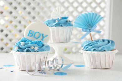 Delicious cupcakes with light blue cream and toppers for baby shower on white table