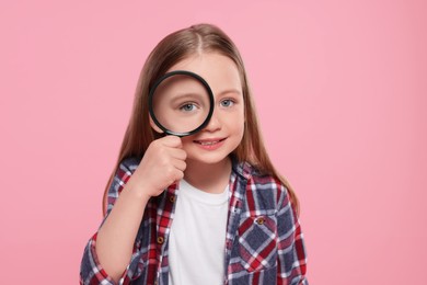 Cute little girl looking through magnifier on pink background