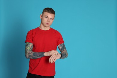 Photo of Young man with tattoos and wristwatch on light blue background. Space for text