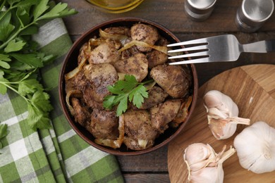 Photo of Tasty fried chicken liver with onion and parsley served on wooden table, flat lay