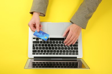 Photo of Online payment. Woman using credit card and laptop at yellow table, top view