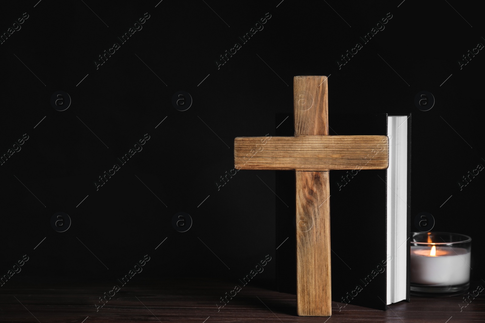 Photo of Cross, Bible and burning candle on wooden table, space for text. Christian religion