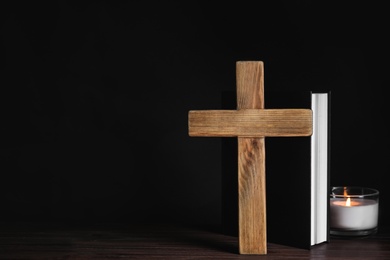 Photo of Cross, Bible and burning candle on wooden table, space for text. Christian religion