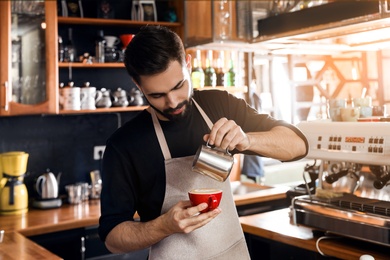 Photo of Barista pouring milk into cup of coffee in shop