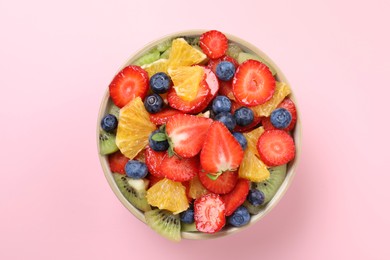 Photo of Yummy fruit salad in bowl on pink background, top view
