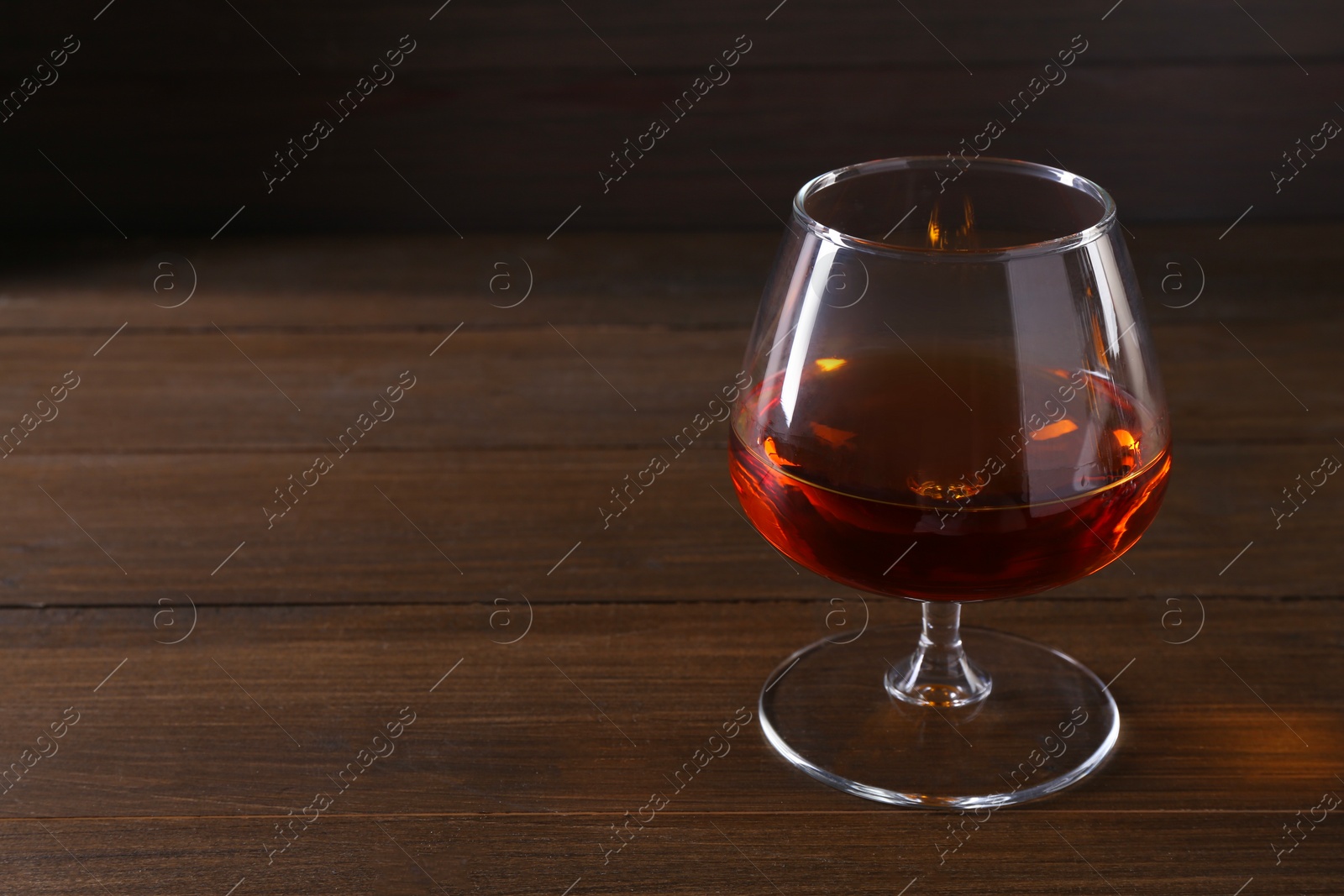 Photo of Delicious liqueur in glass on wooden table. Space for text