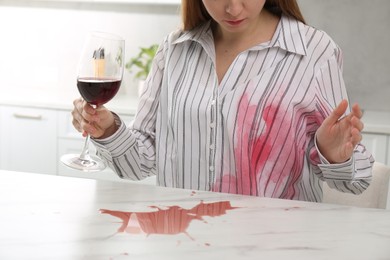 Photo of Woman with spilled wine over her shirt and marble table in kitchen, closeup