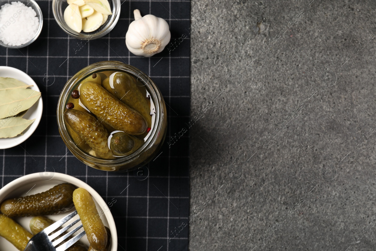 Photo of Tasty pickled cucumbers and spices on grey textured table, top view. Space for text