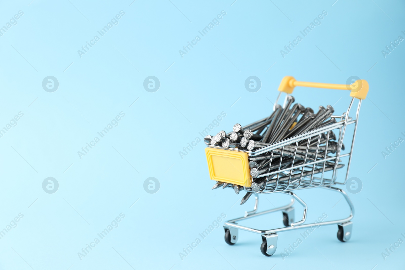 Photo of Metal nails in shopping cart on light blue background, space for text