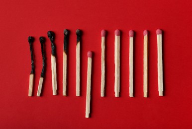 Burnt and whole matches on red background, flat lay. Stop destruction concept