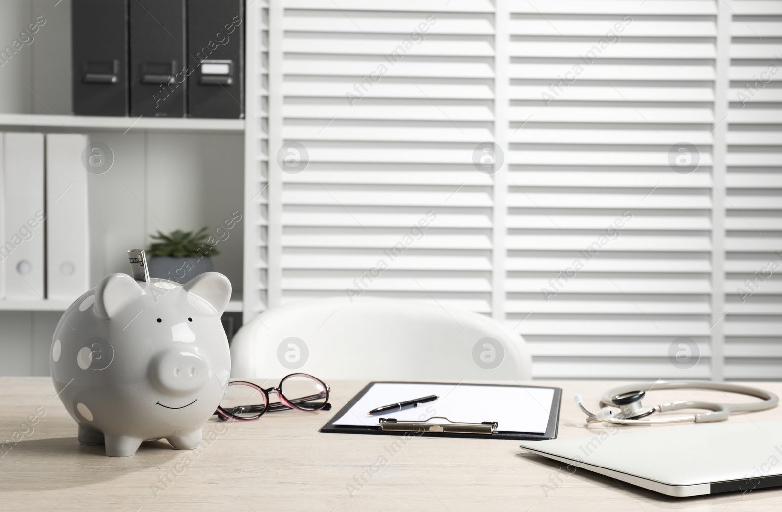 Photo of Piggy bank, glasses, stethoscope and clipboard on wooden table in hospital. Medical insurance