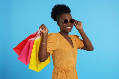 Photo of Happy young woman in stylish sunglasses with shopping bags on light blue background