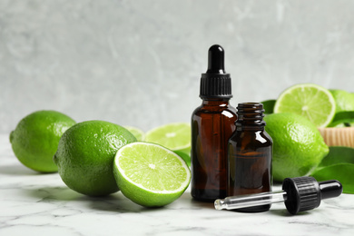 Photo of Lime essential oil and citrus fruits on marble table