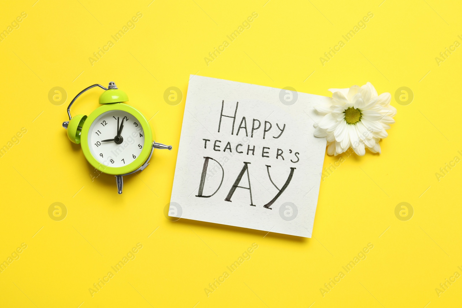 Photo of Flat lay composition of card with inscription HAPPY TEACHER'S DAY, flower and alarm clock on yellow background