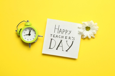 Photo of Flat lay composition of card with inscription HAPPY TEACHER'S DAY, flower and alarm clock on yellow background