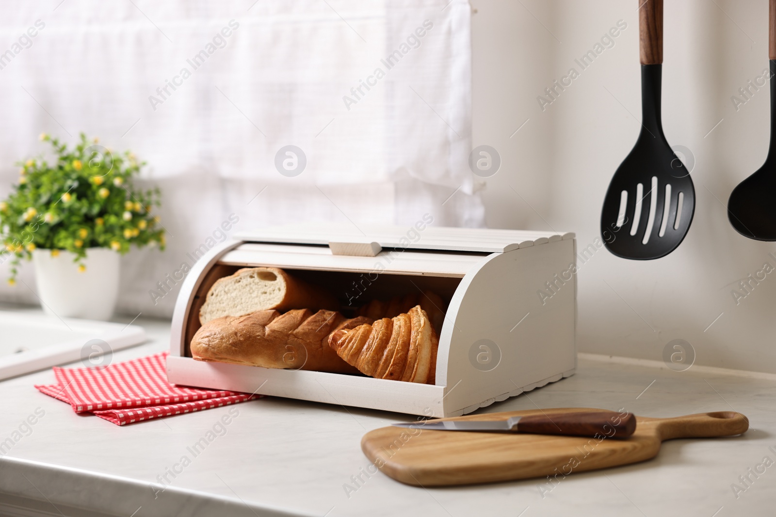 Photo of Wooden bread basket with freshly baked loaves on white marble table in kitchen