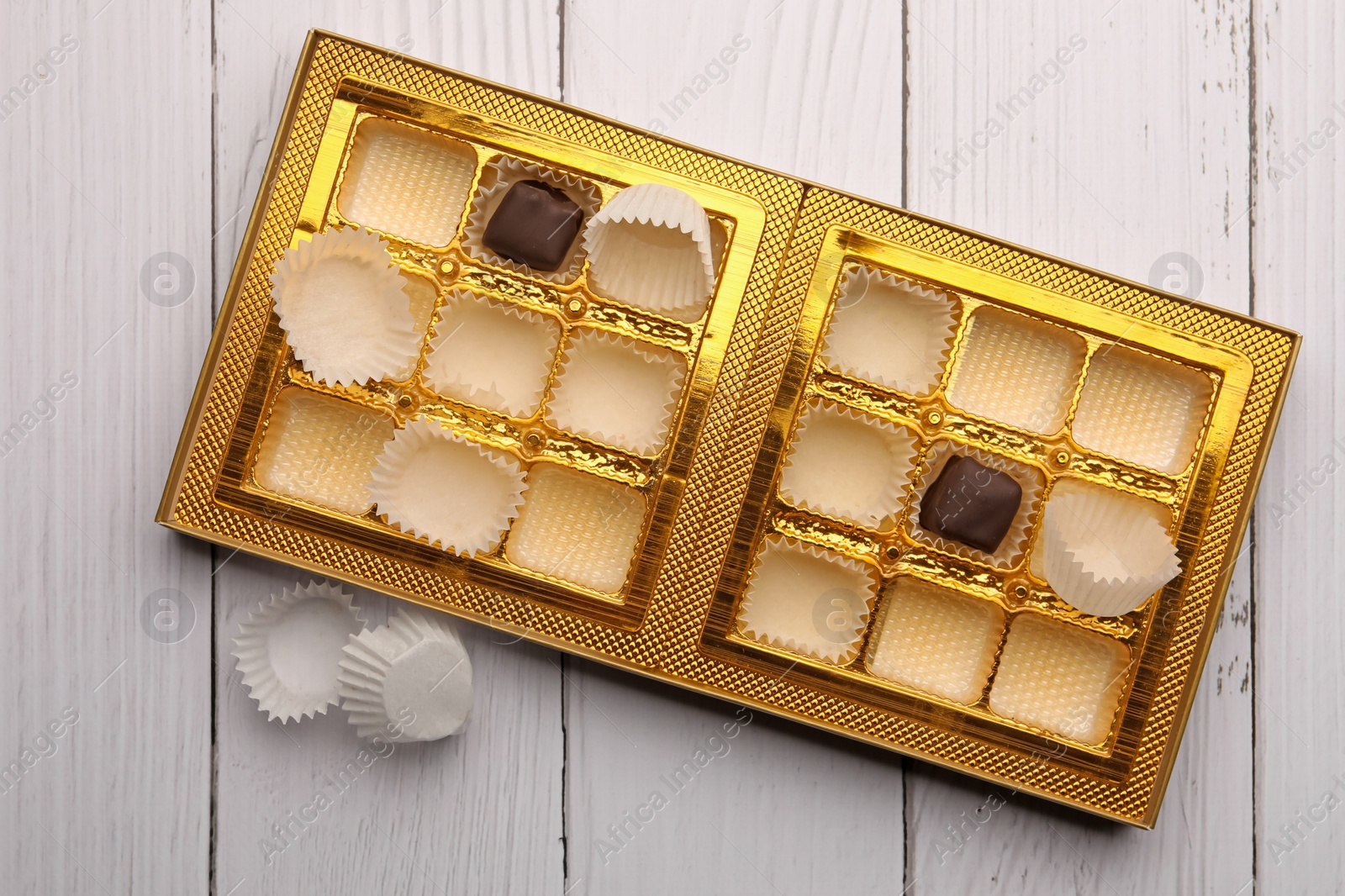 Photo of Partially empty box of chocolate candies on white wooden table, top view