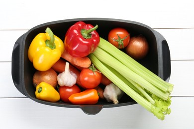 Photo of Black pot with fresh vegetables on white wooden table, top view