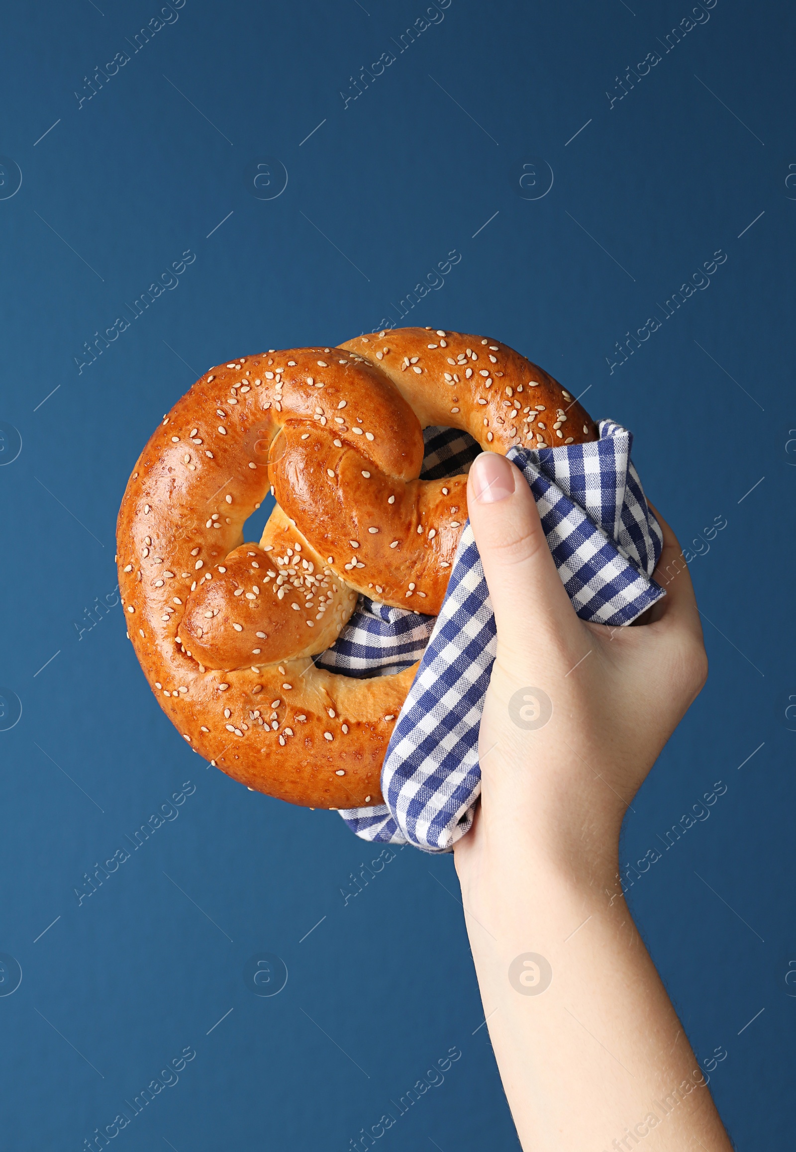 Photo of Woman with tasty freshly baked pretzel on blue background, closeup 