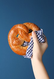 Photo of Woman with tasty freshly baked pretzel on blue background, closeup 