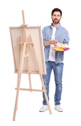 Photo of Man painting with brush against white background. Using easel to hold canvas