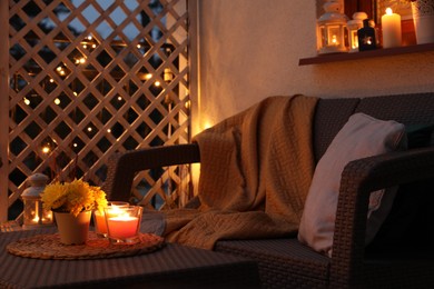 Photo of Beautiful view of garden furniture with pillow, soft blanket and burning candles at balcony