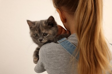 Little girl with kitten on light background, back view. Childhood pet