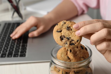 Photo of Office worker taking chocolate chip cookie from jar at workplace, closeup