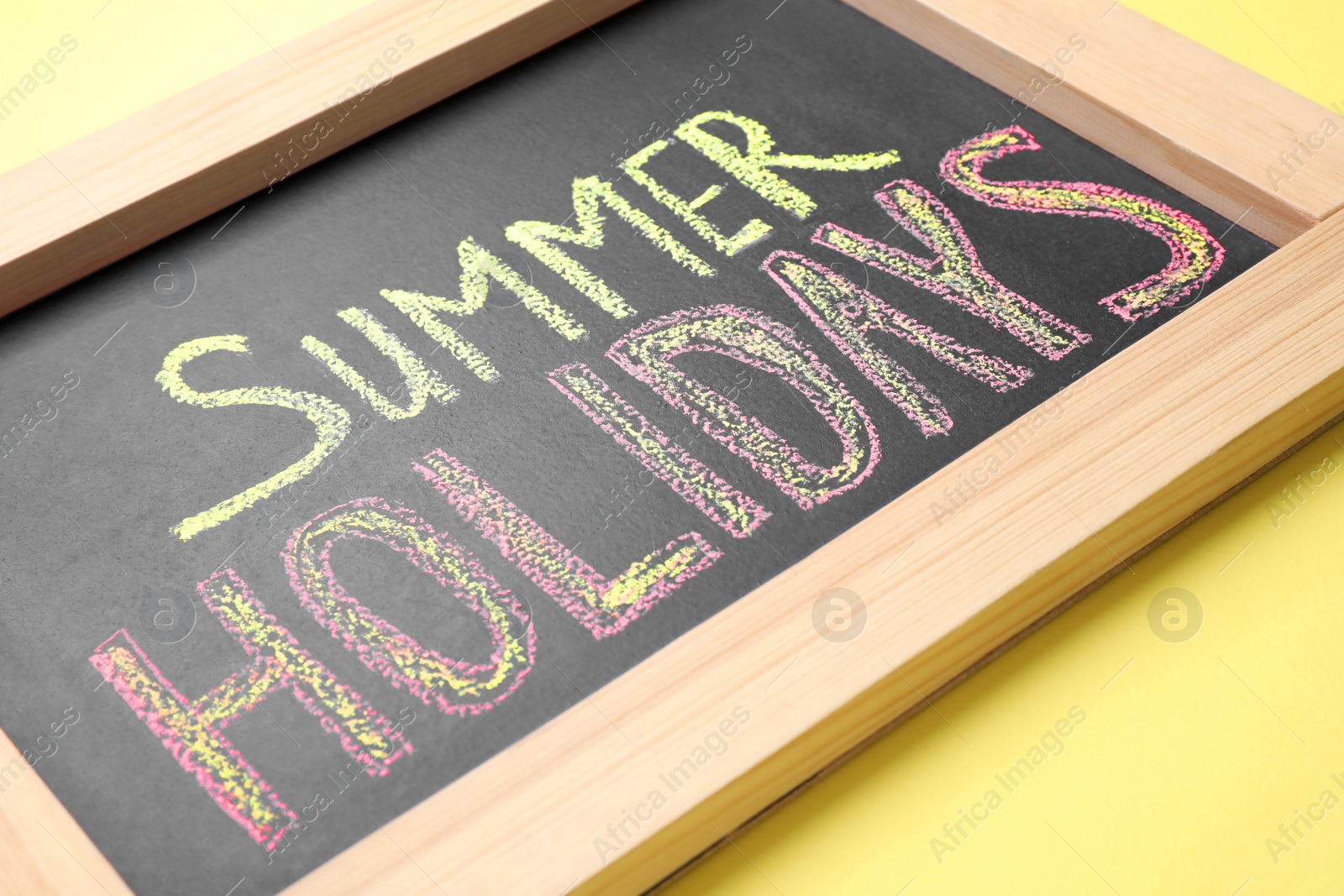 Photo of Chalkboard with phrase SUMMER HOLIDAYS on yellow background, closeup. School's out