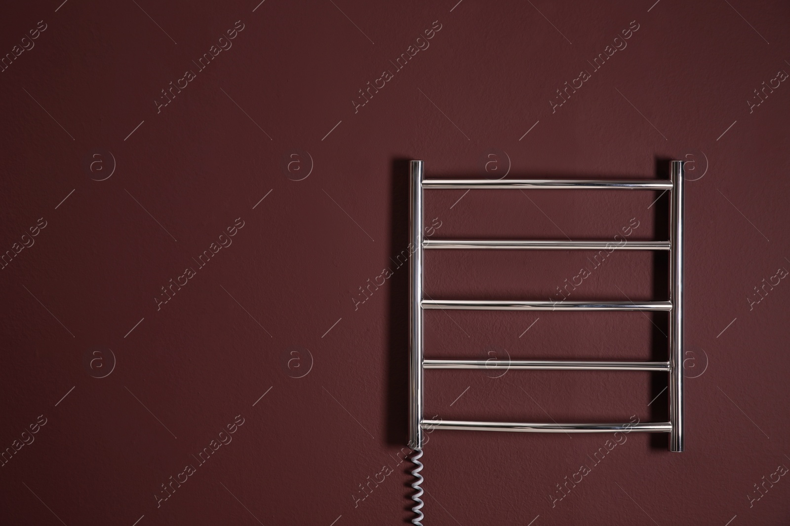 Photo of Modern heated towel rail on dark wall. Space for text