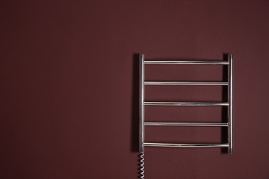 Photo of Modern heated towel rail on dark wall. Space for text