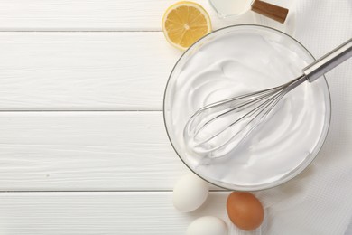 Bowl with whipped cream, whisk and ingredients on white wooden table, flat lay. Space for text