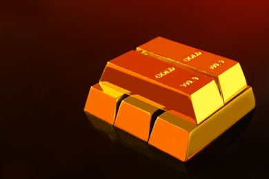Photo of Precious shiny gold bars on mirror surface, space for text