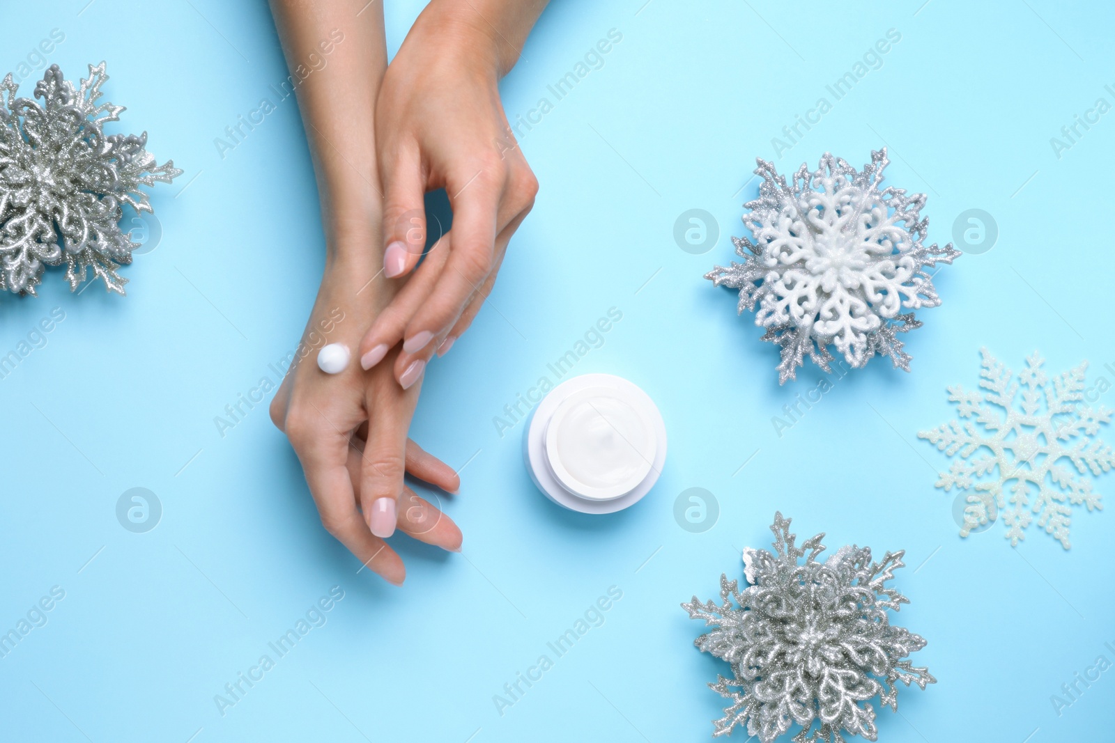 Photo of Woman applying cream onto hand on light blue background, top view