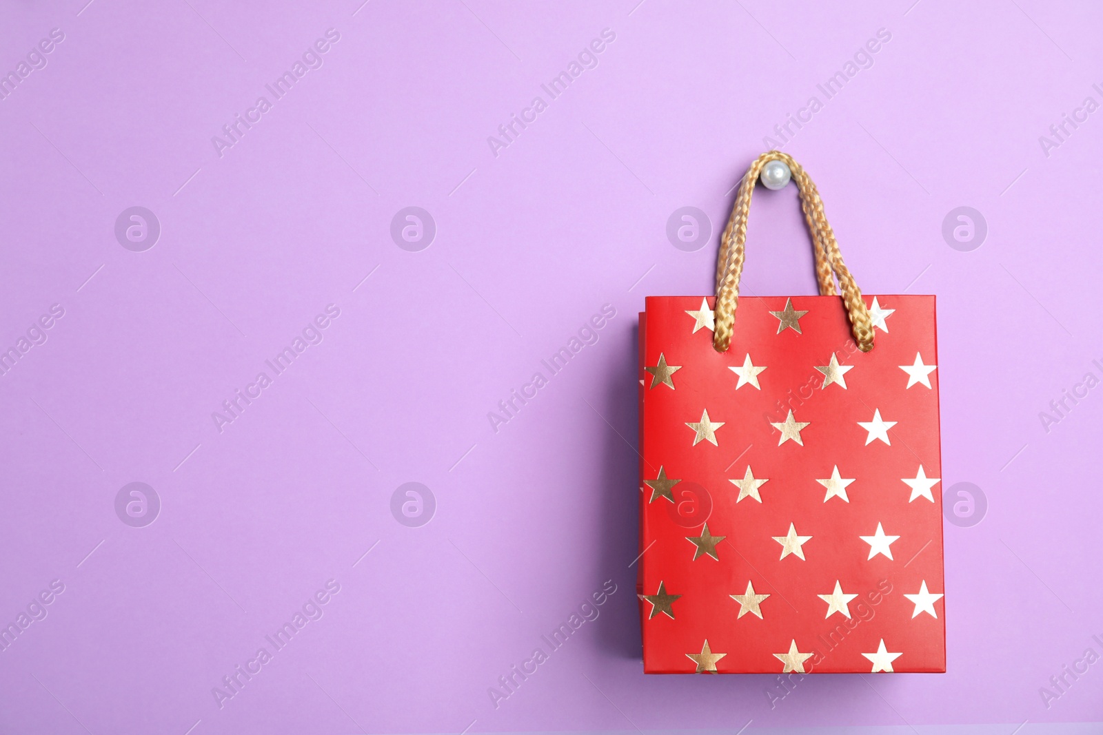 Photo of Red shopping paper bag with star pattern on violet background, space for text